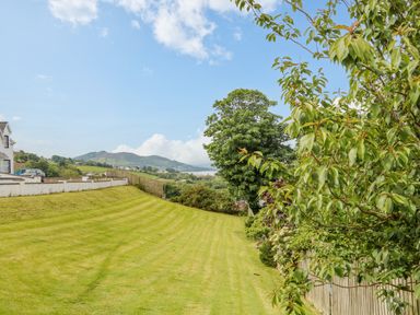 A grassy yard with trees and a fence overlooking hills and houses at 12 Hillview in Ludden near Buncrana