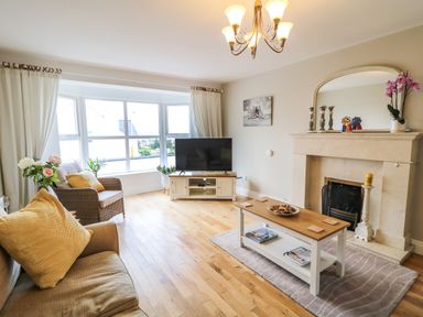 A living room with a sofa, armchair, coffee table, television, fireplace, and large window at 12 Hillview Ludden near Buncrana