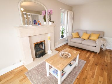 A living room with a beige sofa with yellow cushions a wooden coffee table and a beige fireplace at 12 Hillview Ludden near Buncrana