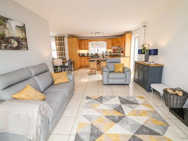 A living room with grey sofas yellow cushions a geometric rug and a kitchen with wooden cabinets at 12 Hillview Ludden near Buncrana