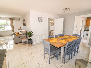 A dining area with a wooden table and eight chairs next to a living room with a sofa and window at 12 Hillview Ludden near Buncrana