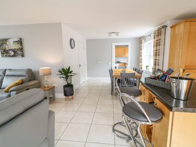 An open-plan living area with grey sofas a dining table with chairs bar stools and a kitchen in the background at 12 Hillview Ludden near Buncrana