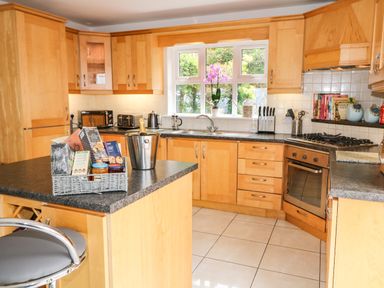 A kitchen with wooden cabinets a countertop island with food items a gas stove an oven and a window with plants at 12 Hillview in Ludden near Buncrana