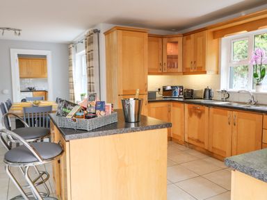 A kitchen with wooden cabinets and granite countertops featuring a kitchen island with two stools and a basket of groceries at 12 Hillview in Ludden near Buncrana
