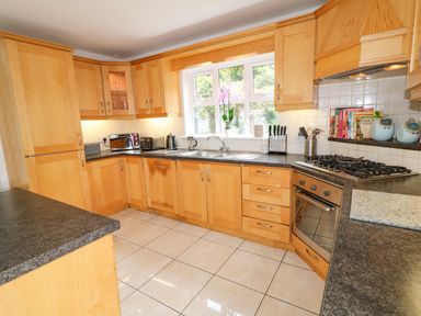 A kitchen with wooden cabinets black countertops a gas stove a sink and tiled floor at 12 Hillview Ludden near Buncrana