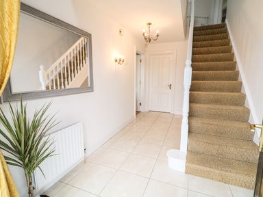A hallway with a carpeted staircase a large mirror a wall sconce a plant and tiled floor at 12 Hillview Ludden near Buncrana