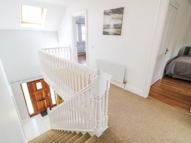 A staircase with white banisters leading to a hallway with carpet and doors to bedrooms at 12 Hillview Ludden near Buncrana