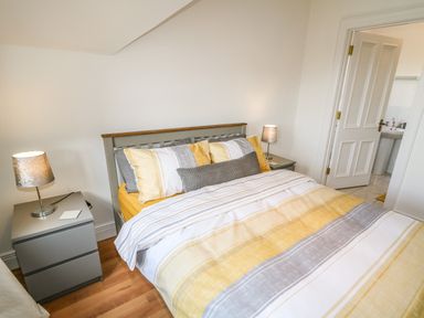 A bedroom with a bed with striped yellow and gray bedding two gray nightstands with lamps and a door leading to a bathroom at 12 Hillview Ludden near Buncrana
