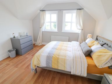 A bedroom with a bed with striped bedding and pillows next to two windows and a gray chest of drawers at 12 Hillview in Ludden near Buncrana