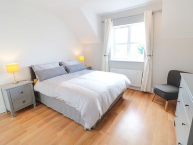 A bedroom with a double bed side tables and lamps a dresser and a chair at 12 Hillview Ludden near Buncrana