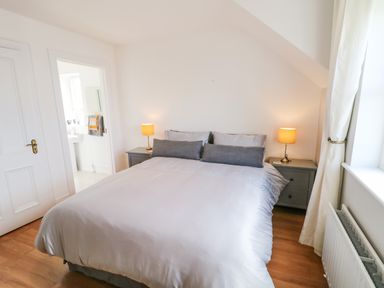 A bedroom with a double bed two bedside tables and lamps wooden floor and a window with curtains at 12 Hillview Ludden near Buncrana