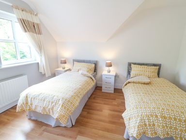 A bedroom with two single beds yellow patterned bedding two white nightstands with lamps and a window with curtains at 12 Hillview in Ludden near Buncrana