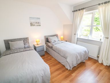 A bedroom with two single beds a nightstand with two lamps a window with curtains and wooden floor at 12 Hillview Ludden near Buncrana