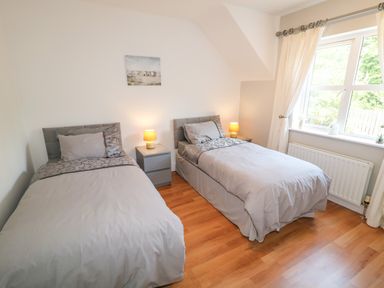 A bedroom with two single beds bedside tables with lamps a window and a painting on the wall at 12 Hillview in Ludden near Buncrana