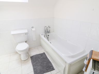 A bathroom with a toilet, bathtub, toilet paper holder, grey bath mat, and towels on a radiator at 12 Hillview Ludden near Buncrana
