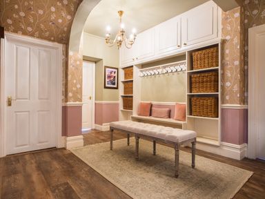 An entryway with white built-in shelves and hooks a cushioned bench wicker baskets pink pillows and a chandelier at Swinside Lodge in Newlands Valley near Keswick