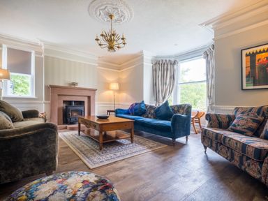 A living room with sofas a wooden coffee table a fireplace and windows with curtains at Swinside Lodge in Newlands Valley near Keswick