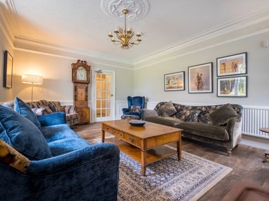 A living room with blue and floral sofas a wooden coffee table a grandfather clock and framed pictures on the wall at Swinside Lodge in Newlands Valley near Keswick