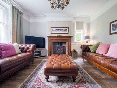 A living room with two leather sofas a leather ottoman a fireplace a television and a window at Swinside Lodge in Newlands Valley near Keswick