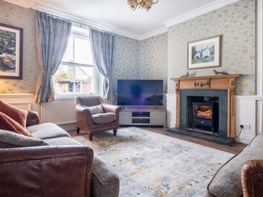 A living room with a sofa an armchair a television on a cabinet a fireplace and patterned curtains at Swinside Lodge in Newlands Valley near Keswick