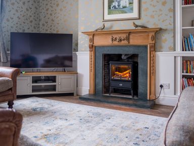 A living room with a fireplace a television on a stand and bookshelves at Swinside Lodge in Newlands Valley near Keswick