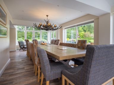 A dining room with a large wooden table surrounded by mixed upholstered chairs and windows showing a garden at Swinside Lodge in Newlands Valley near Keswick