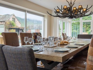 A dining room with a wooden table set with plates and wine glasses and an antler chandelier at Swinside Lodge in Newlands Valley near Keswick