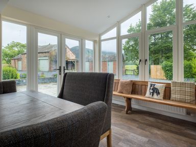 A dining area with a wooden table and upholstered chairs next to large windows and a bench with cushions at Swinside Lodge in Newlands Valley near Keswick