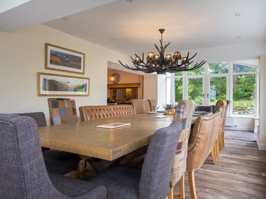 A dining room with a large wooden table surrounded by upholstered chairs and a window with a garden view at Swinside Lodge in Newlands Valley near Keswick