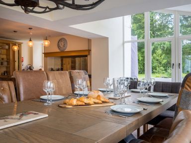 A dining room with a wooden table set with plates and glasses near large windows at Swinside Lodge Newlands Valley near Keswick