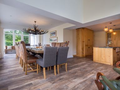 A dining area with a large table surrounded by various chairs next to a kitchen with wooden cabinets and an island at Swinside Lodge in Newlands Valley near Keswick