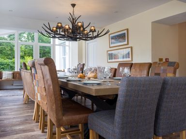A dining room with a long table set with plates and glasses and mixed chairs under a chandelier at Swinside Lodge Newlands Valley near Keswick