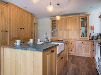 A kitchen with wooden cabinets a large sink an island with mugs and bread at Swinside Lodge in Newlands Valley near Keswick