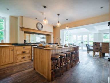 A kitchen with wooden cabinets an island with stools a dining area with chairs and large windows at Swinside Lodge in Newlands Valley near Keswick