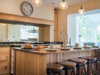A kitchen island with wooden stools cups and plates and a loaf of bread and croissants at Swinside Lodge in Newlands Valley near Keswick