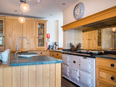 A kitchen with wooden cabinets a white stove a clock on the wall and a countertop with mugs and a sink at Swinside Lodge in Newlands Valley near Keswick