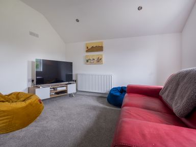 A living room with a red sofa, yellow and blue bean bags, a television on a stand, and two paintings on the wall at Swinside Lodge in Newlands Valley near Keswick