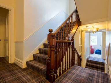 A staircase with wooden railing and plaid carpet leading to a hallway with doors at Swinside Lodge in Newlands Valley near Keswick