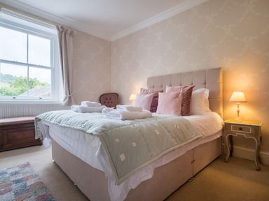 A bedroom with a bed with pillows and folded towels bedside table with lamp window with curtain and chair near the wall at Swinside Lodge in Newlands Valley near Keswick