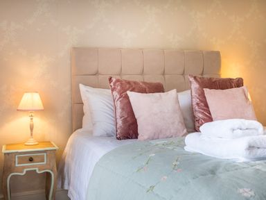A bedroom with a bed with headboard pillows bedside table with lamp and folded towels on bed at Swinside Lodge in Newlands Valley near Keswick