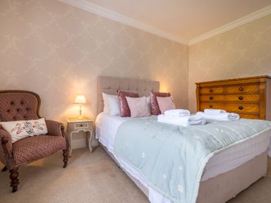 A bedroom with a bed with folded towels pillows an armchair and a wooden dresser at Swinside Lodge in Newlands Valley near Keswick