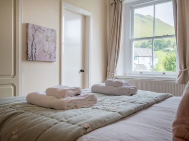 A bedroom with a bed covered with folded white towels near a window showing houses and a hillside outside at Swinside Lodge in Newlands Valley near Keswick