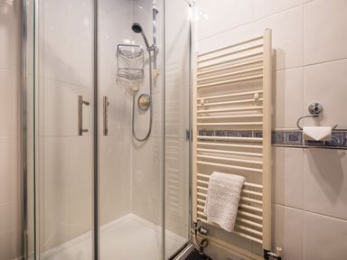 A bathroom with a glass-enclosed shower, chrome showerhead, towel rack with towel, and a toilet paper holder at Swinside Lodge in Newlands Valley near Keswick