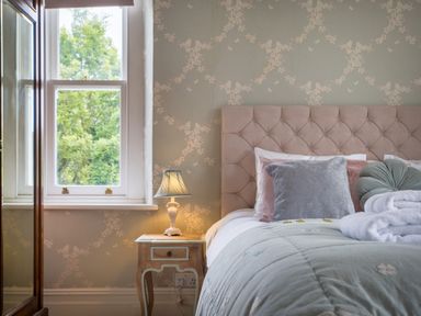 A bedroom with a window, bedside table with a lamp, and a bed with cushions and folded towels at Swinside Lodge in Newlands Valley near Keswick