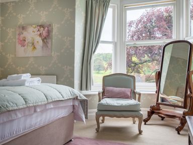 A bedroom with a bed towel stack armchair mirror and window overlooking trees at Swinside Lodge in Newlands Valley near Keswick