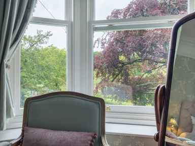 A window view showing green and purple trees with part of a chair and a mirror in a bedroom at Swinside Lodge in Newlands Valley near Keswick