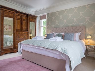 A bedroom with a bed, ornate wooden wardrobe with mirrors, two bedside tables with lamps at Swinside Lodge in Newlands Valley near Keswick