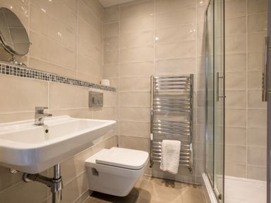 A bathroom with a wall mounted sink and toilet a glass shower enclosure and a towel radiator with a towel at Swinside Lodge in Newlands Valley near Keswick