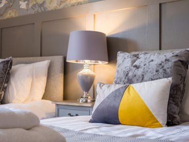 A bedroom with a gray and yellow pillow on a bed next to a gray table lamp at Swinside Lodge in Newlands Valley near Keswick