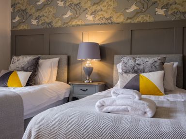 A bedroom with two beds a bedside table with a lamp and patterned wallpaper at Swinside Lodge in Newlands Valley near Keswick